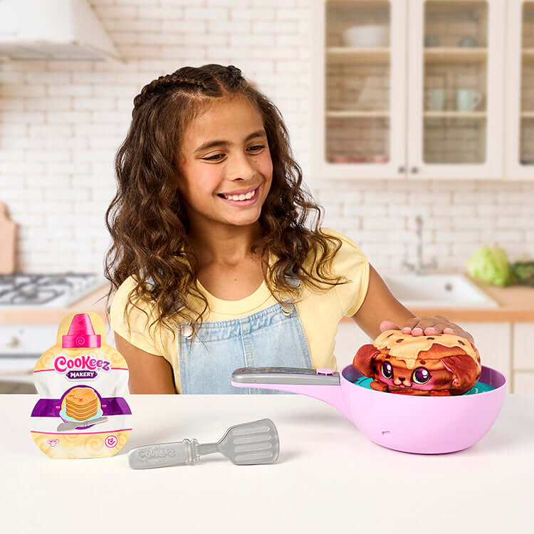 Girl playing with Cookeez Makery Pancake Treatz Playset in kitchen, revealing scented plush pancake toy.